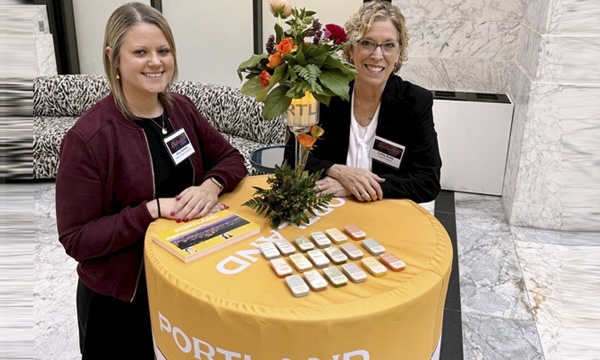 Two women stand at the Travel Portland table ready to greet people