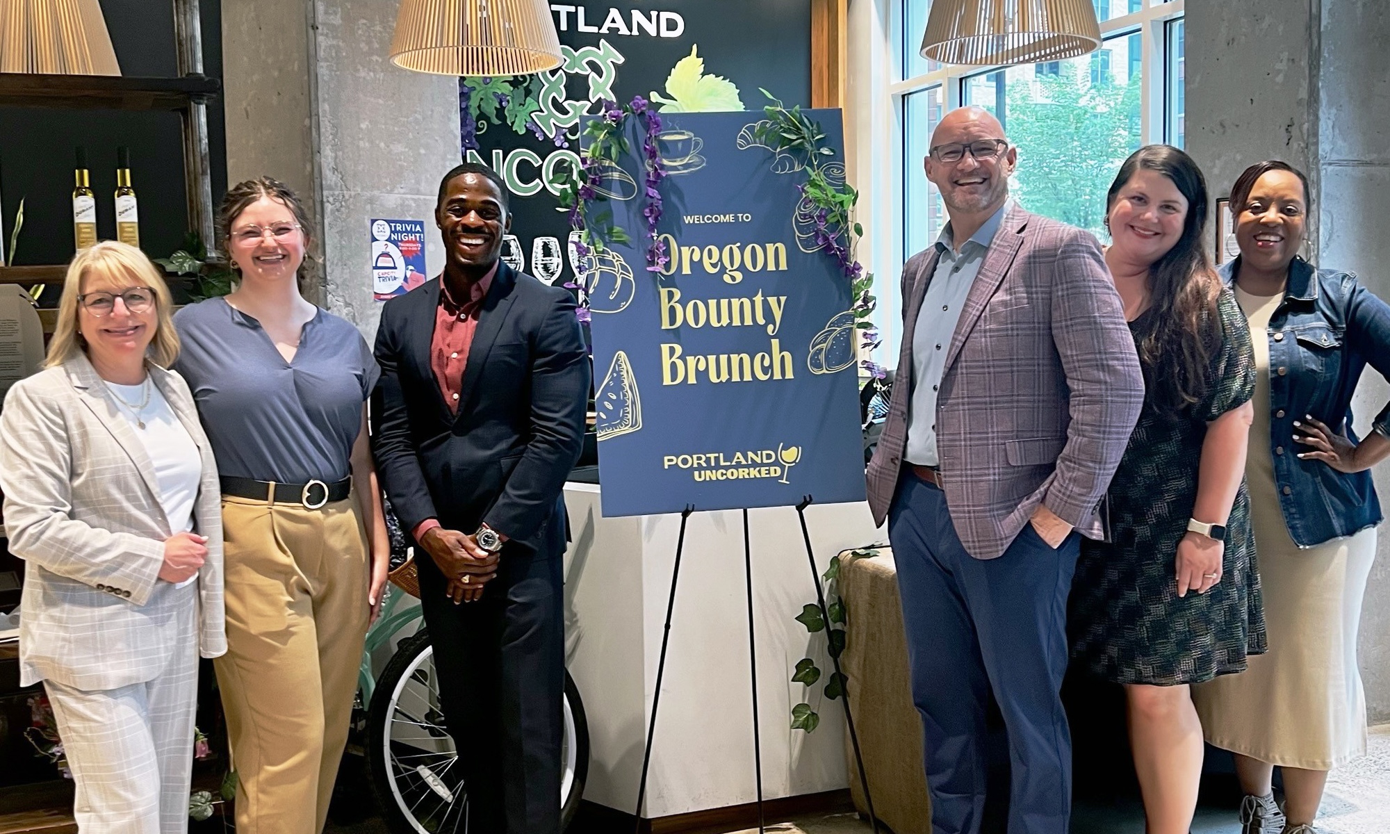 Six people pose next to the Oregon Bounty Brunch sign