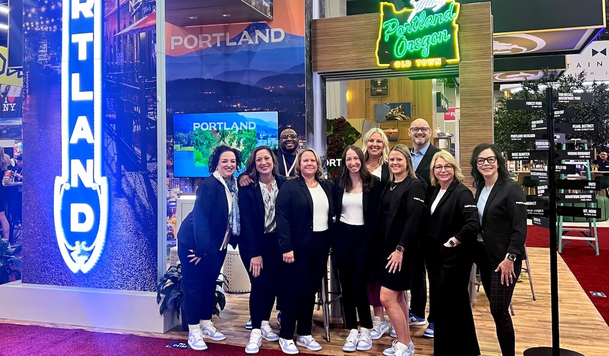 The Travel Portland sales team gathers in front of Portland signage for a photo at IMEX